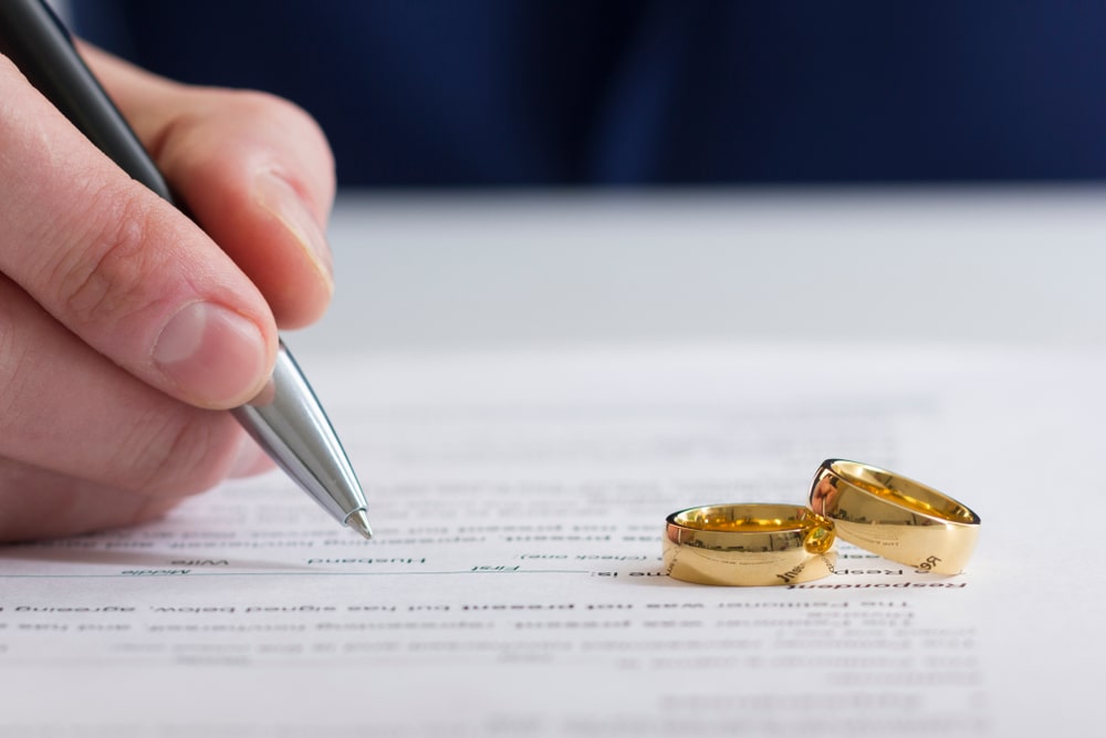 Person Writing On A Paper Next To Two Wedding Rings